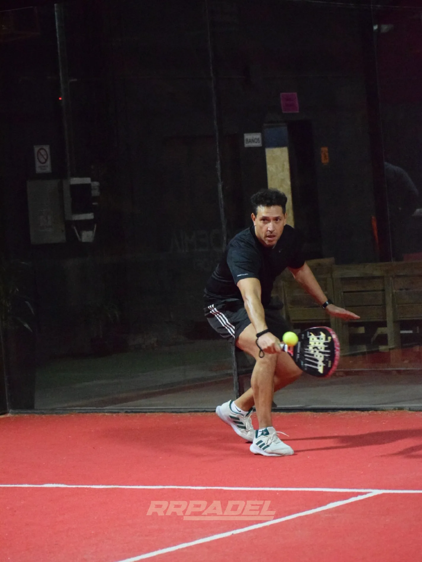 Jugador de RR devolviendo una pelota en la cancha indoor roja; marca RR Pádel en la fotografía